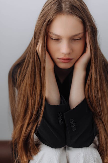 Portrait of a young woman covering her ears, appearing overwhelmed with emotion.