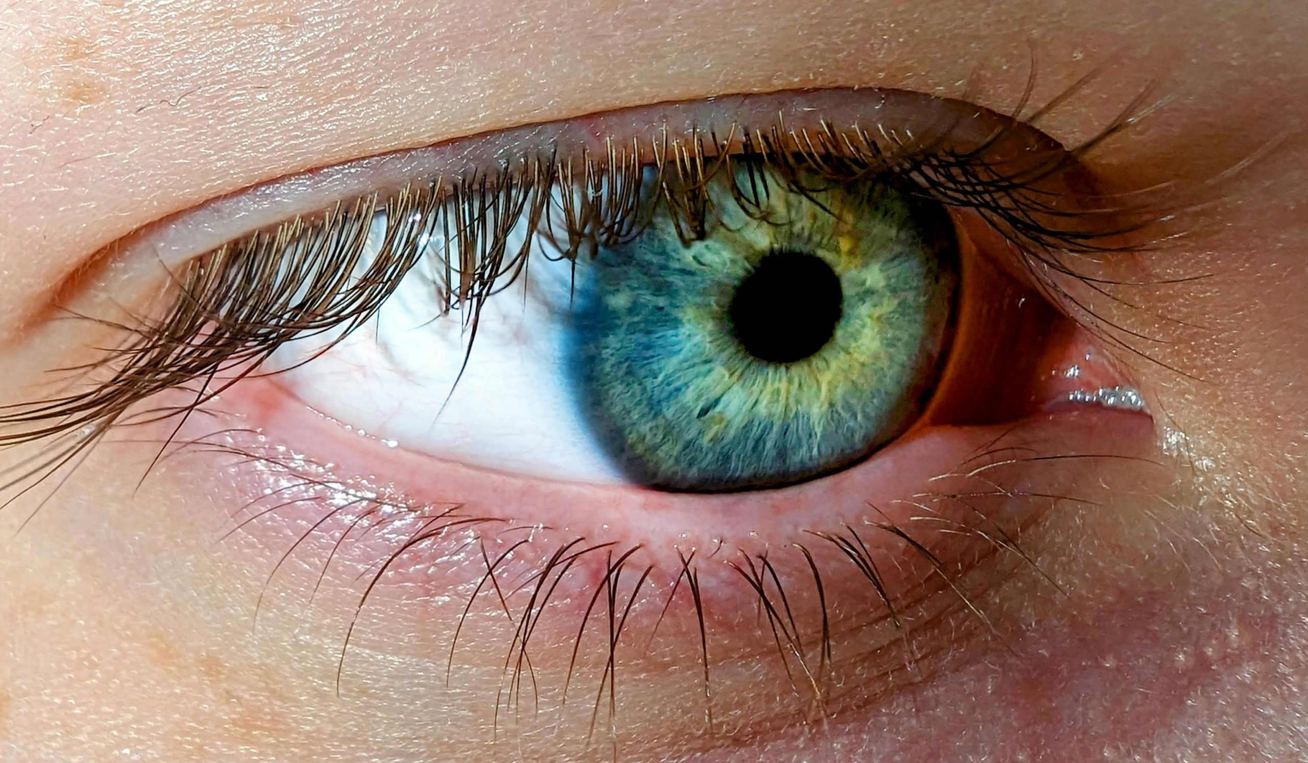 Detailed macro shot of a blue-green human eye showcasing intricate details of the iris.