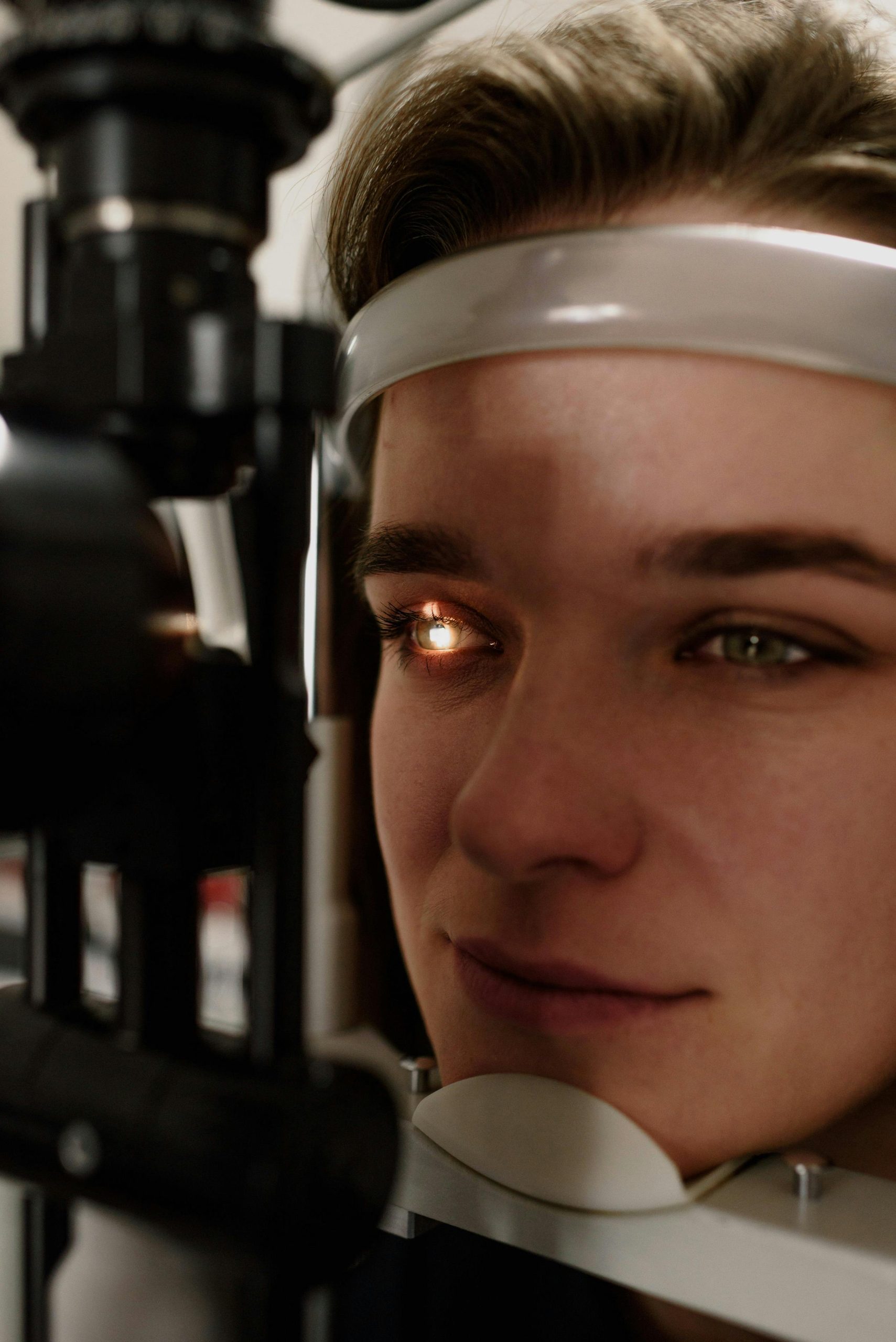 Headshot of concentrated female patient having eyesight examination with special optical equipment while sitting at professional slit lamp in clinic