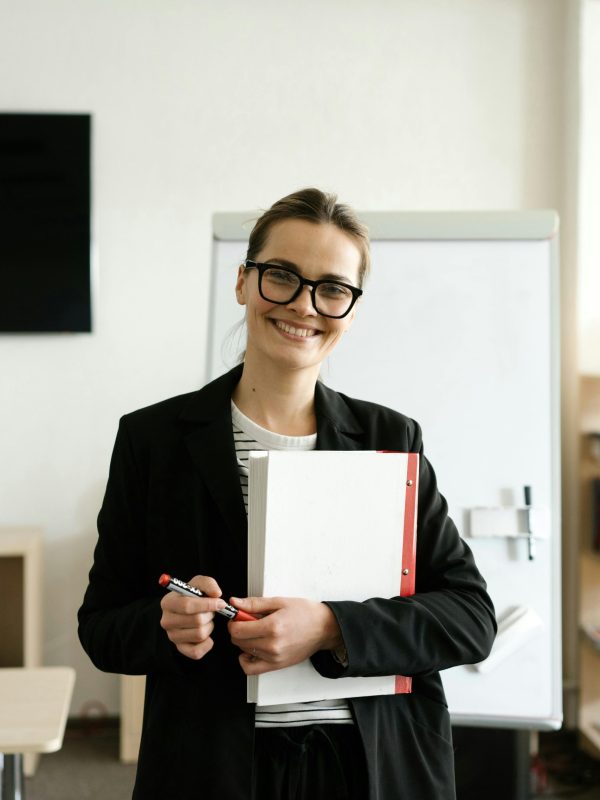 Professional woman in a classroom holding documents and smiling warmly.